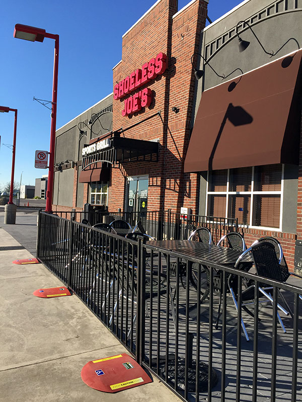 Black picket fence with orange safety ramps encloses a restaurant patio.