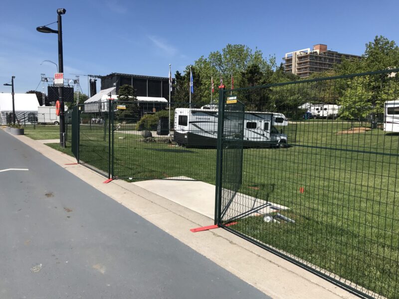 Dark green temporary fencing encloses a field with RVs parked in it