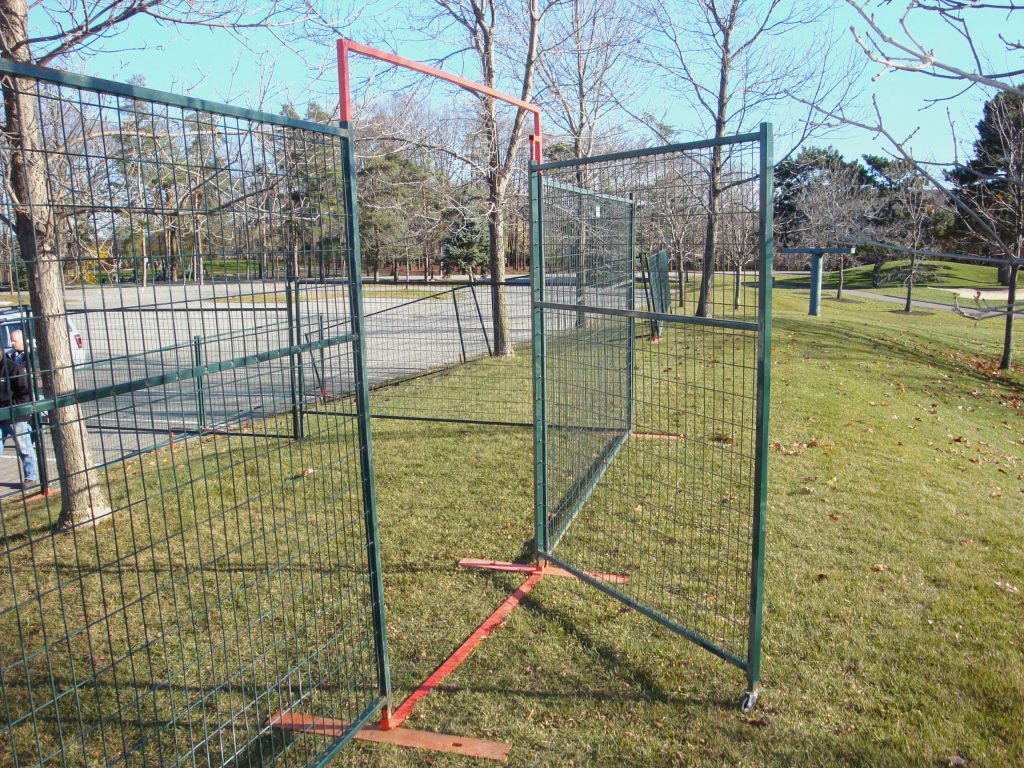 Temporary fencing with an integrated swing gate is seen in a park.