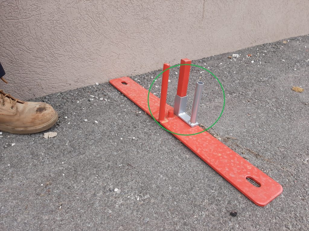 A rectangular metal fence base with one square upright peg and one round upright peg, and a u-shaped sliding gate guide installed on the square peg