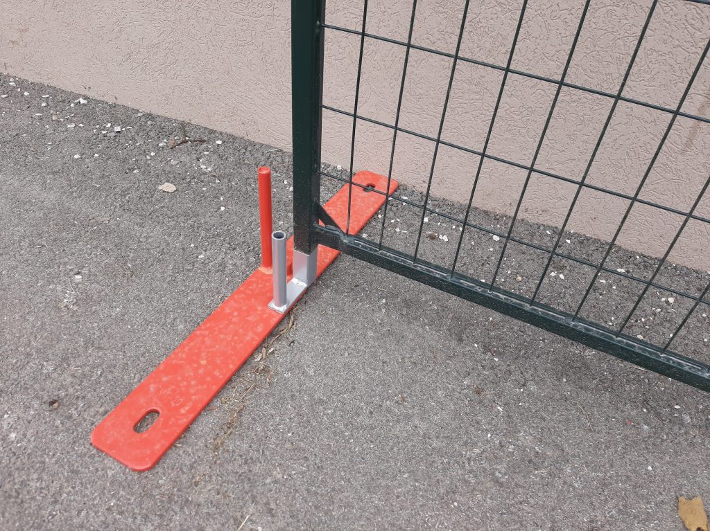 A dark green steel temporary fence panel sits on top of a u-shaped sliding gate guide, which has been installed on a metal fence base perpendicular to the fence panel