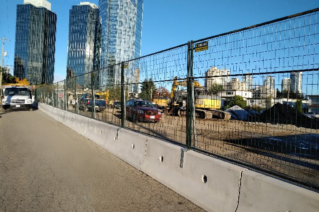 Temporary fencing mounted onto concrete barriers surrounds a construction site