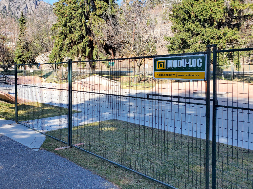 A 6' high dark green steel temporary fence in front of a park.