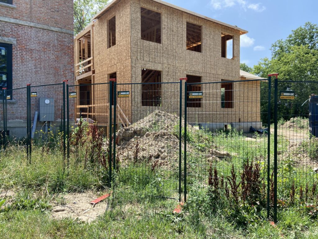 A house under construction is surrounded by a temporary barricade made of steel mesh fence panels.