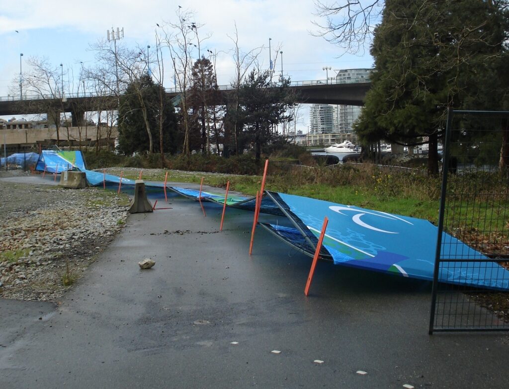 A line of temporary fencing with screening fallen over onto a bike path in a park.